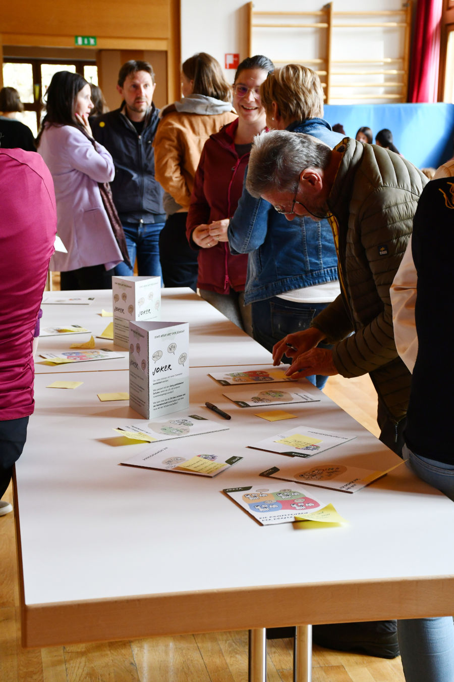 A picture that shows adults that read flyers and hand-outs that are spread on a long table.